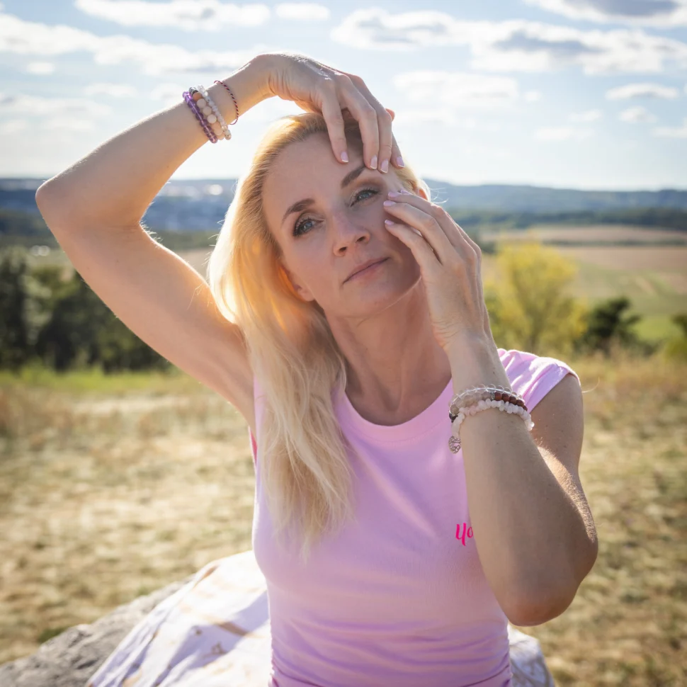 Certifikovaná lektorka Martina Bajerová z programu Facelift Yoga Experience předvádí jemnou techniku pro osvěžení oblasti kolem očí během cvičení v přírodě.